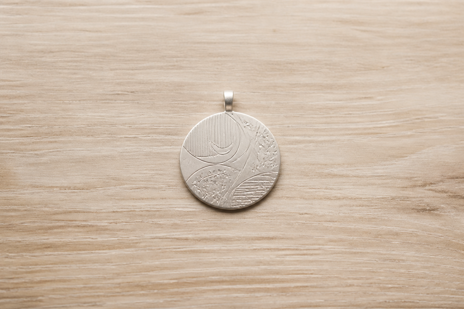 Médaille bijou ronde ornée de motifs gravés abstraits sur du bois clair